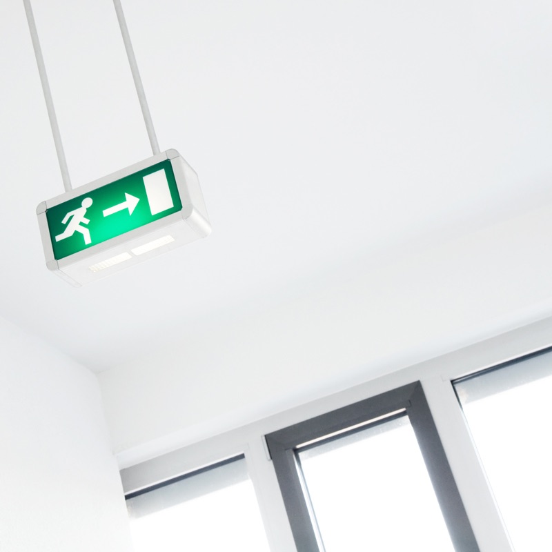 An illuminated green emergency exit sign suspended below the ceiling of a commercial interior