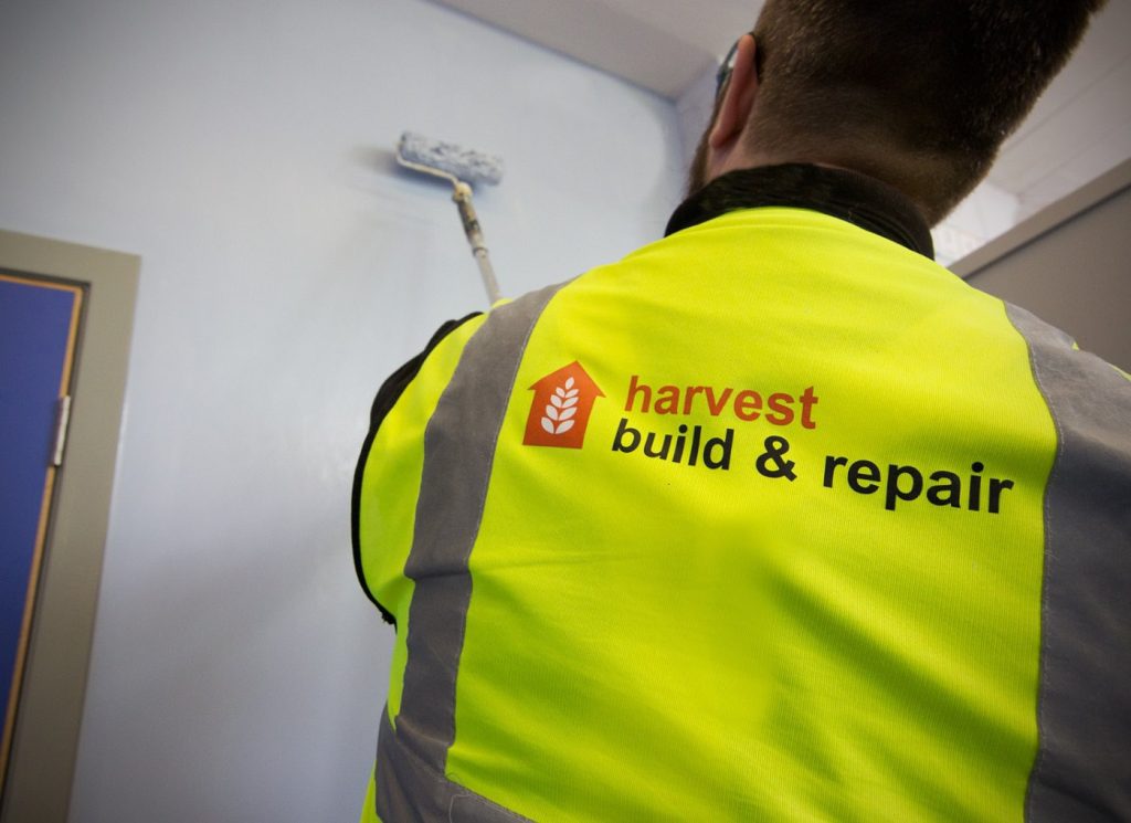 A Harvest Contracts painter in a branded hi-vis vest rolling paint onto an interior wall